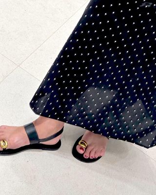 British fashion influencer Lucy Alston poses in a sheer polka-dot dress and black flat sandals with toe ring that has sculptural metal details