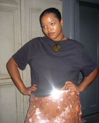 Woman in cord necklace, black t-shirt, and sequin skirt.